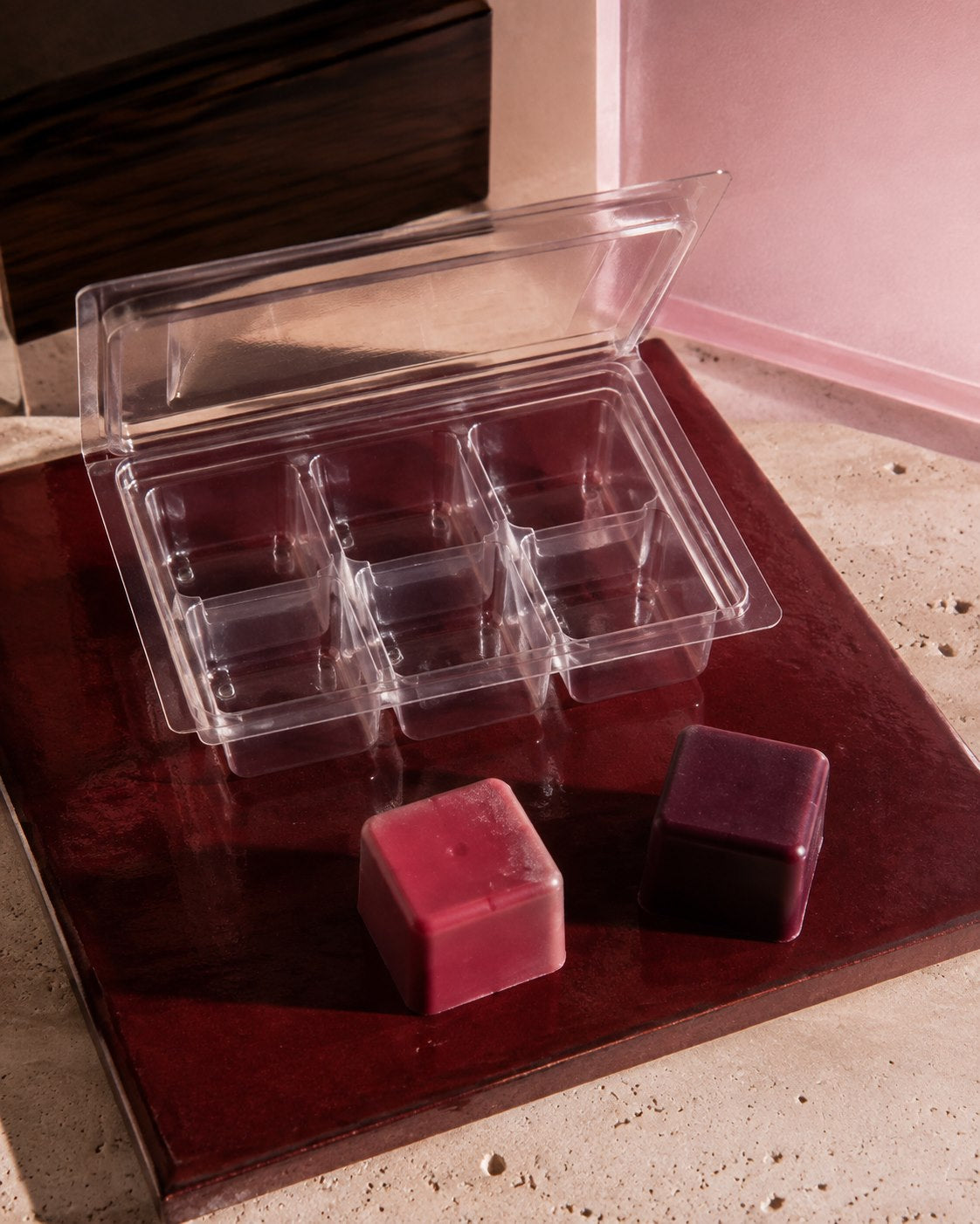 Editorial still life of a wax melt clamshell and berry-toned wax cubes